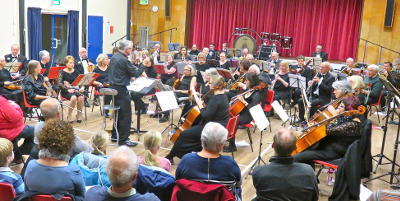 An orchestra playing led by a composer with an audience watching.