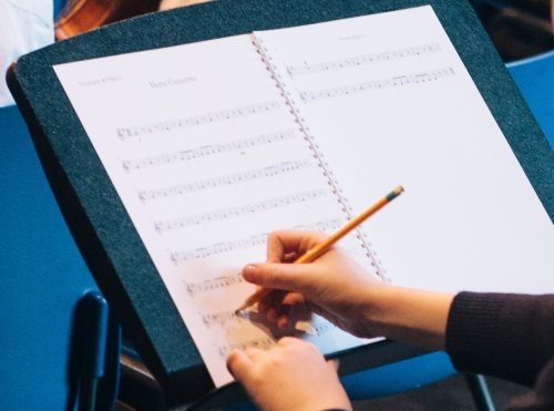 Close up image of a young person's hands annotating sheet music with a pencil.