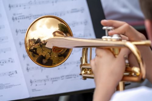 A close up of a hand playing a trumpet. There is sheet music in the background.