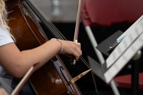 A close up of a hand playing a cello. There is sheet music in the background.